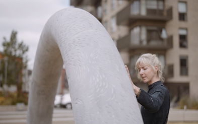 Artist Ruth Lyons beside her large white curved sculpture at a Cairn development