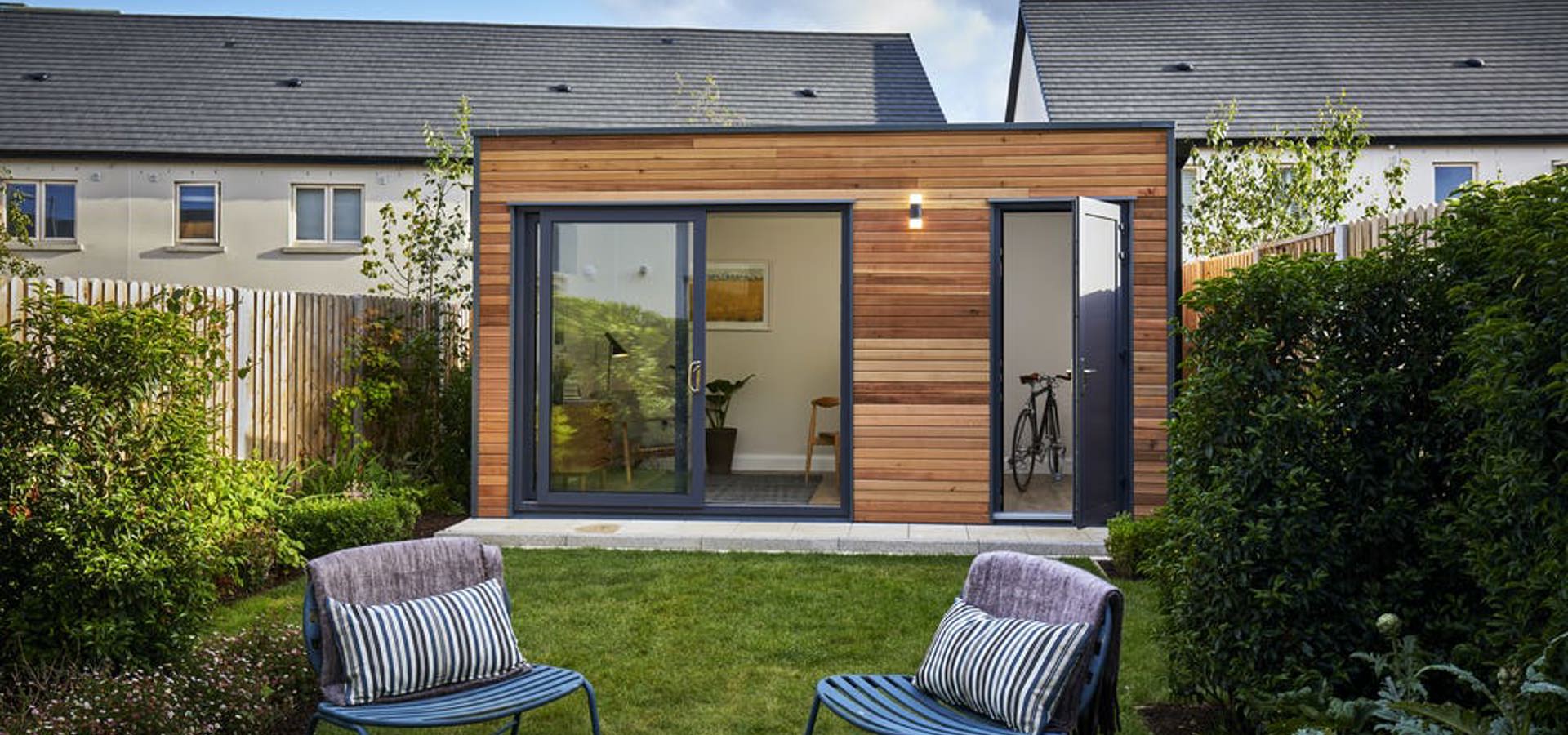 Garden office pod with glazed doors and two chairs on the lawn of a back garden