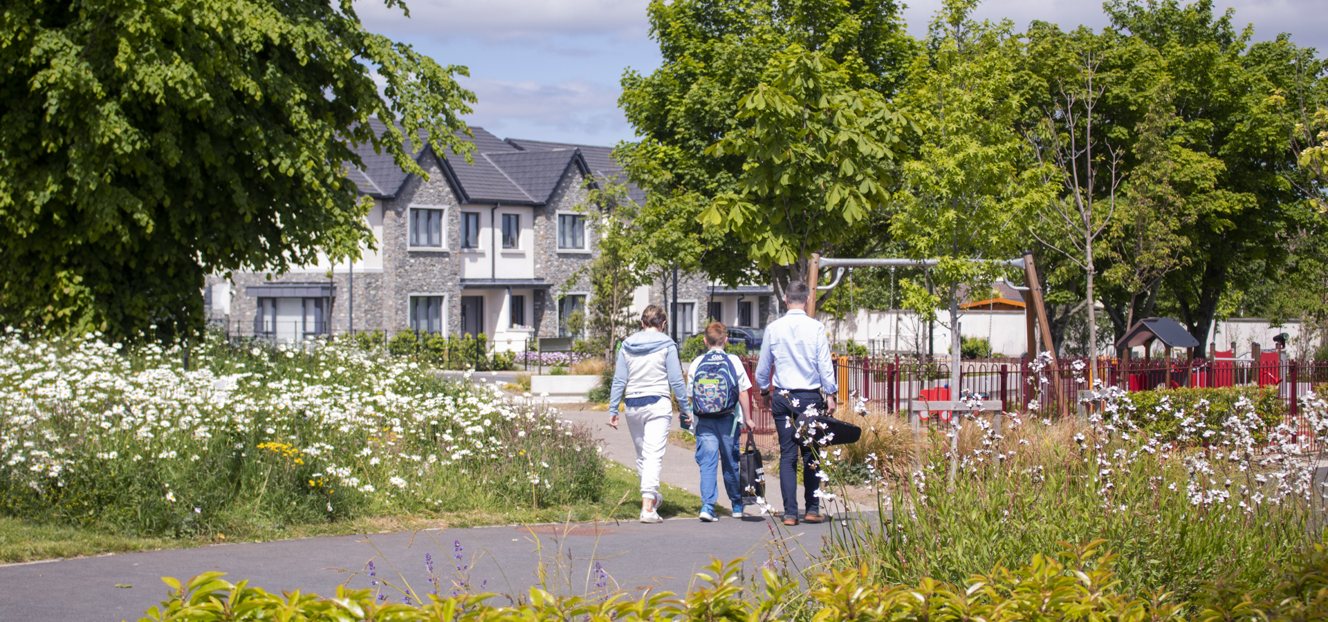 Residents walking a path past wildflower planting and new homes at a Cairn development