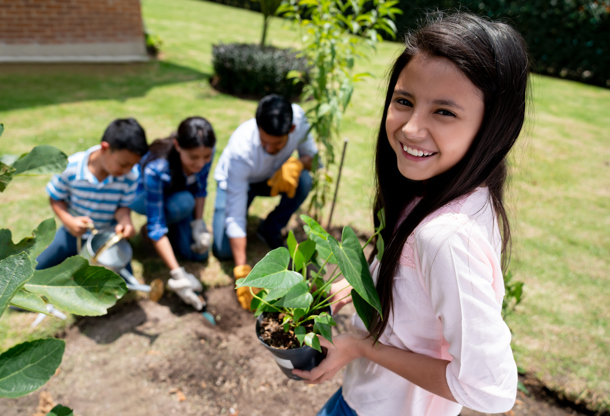 Children planting a young tree in a garden while an adult helps