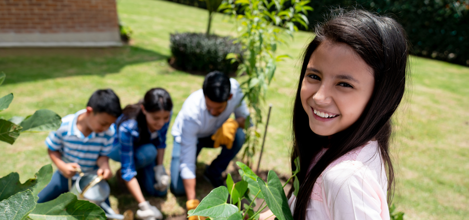 Children planting a young tree in a garden while an adult helps