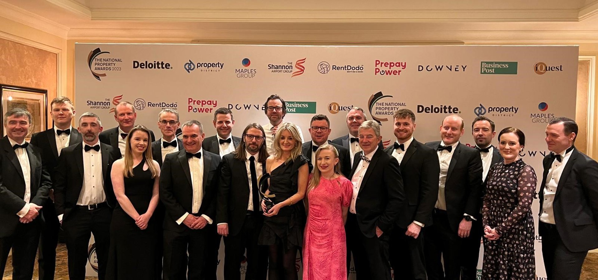 Cairn team in black tie with their award in front of an awards sponsors' backdrop