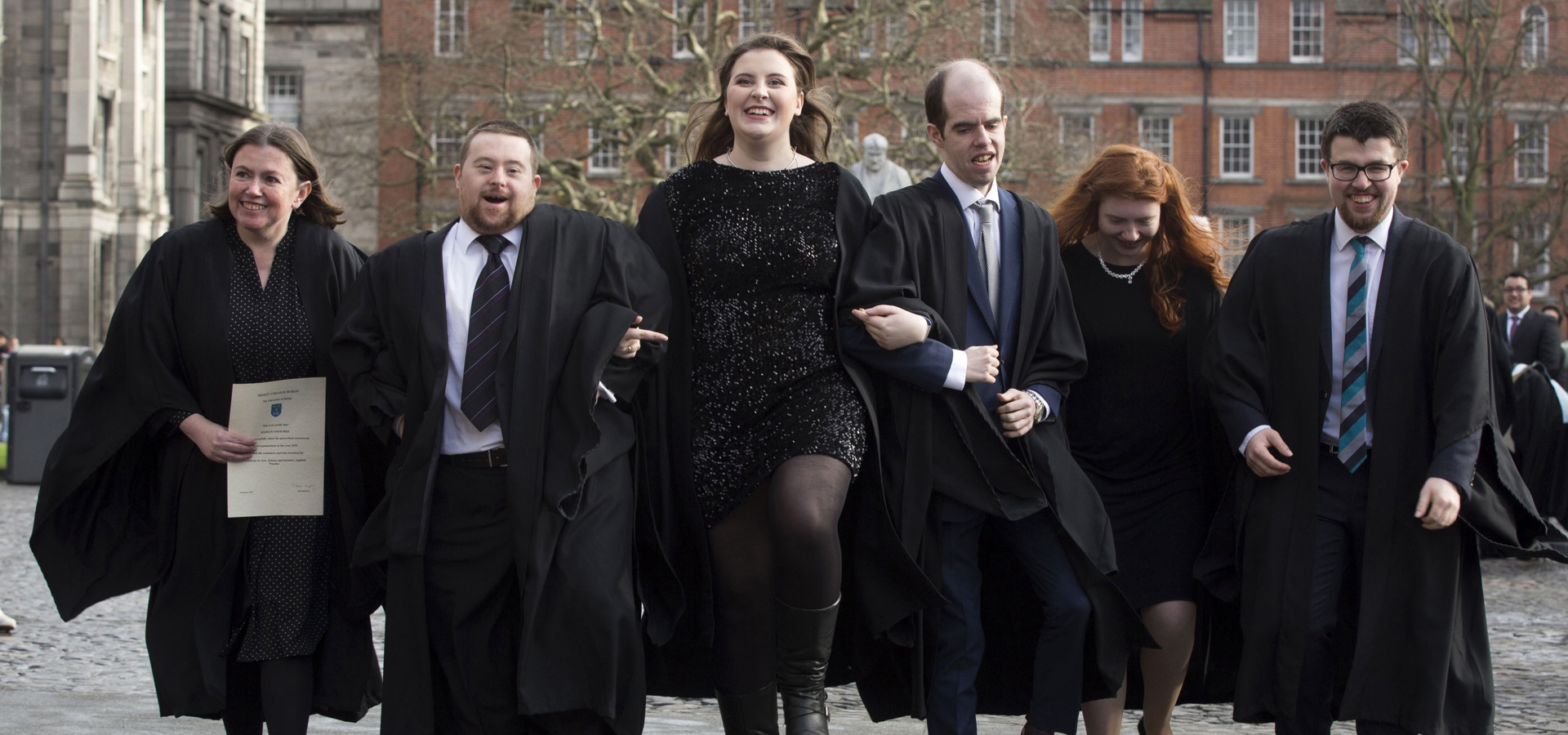 Group in academic gowns walking outside Trinity College Dublin at a TCPID graduation
