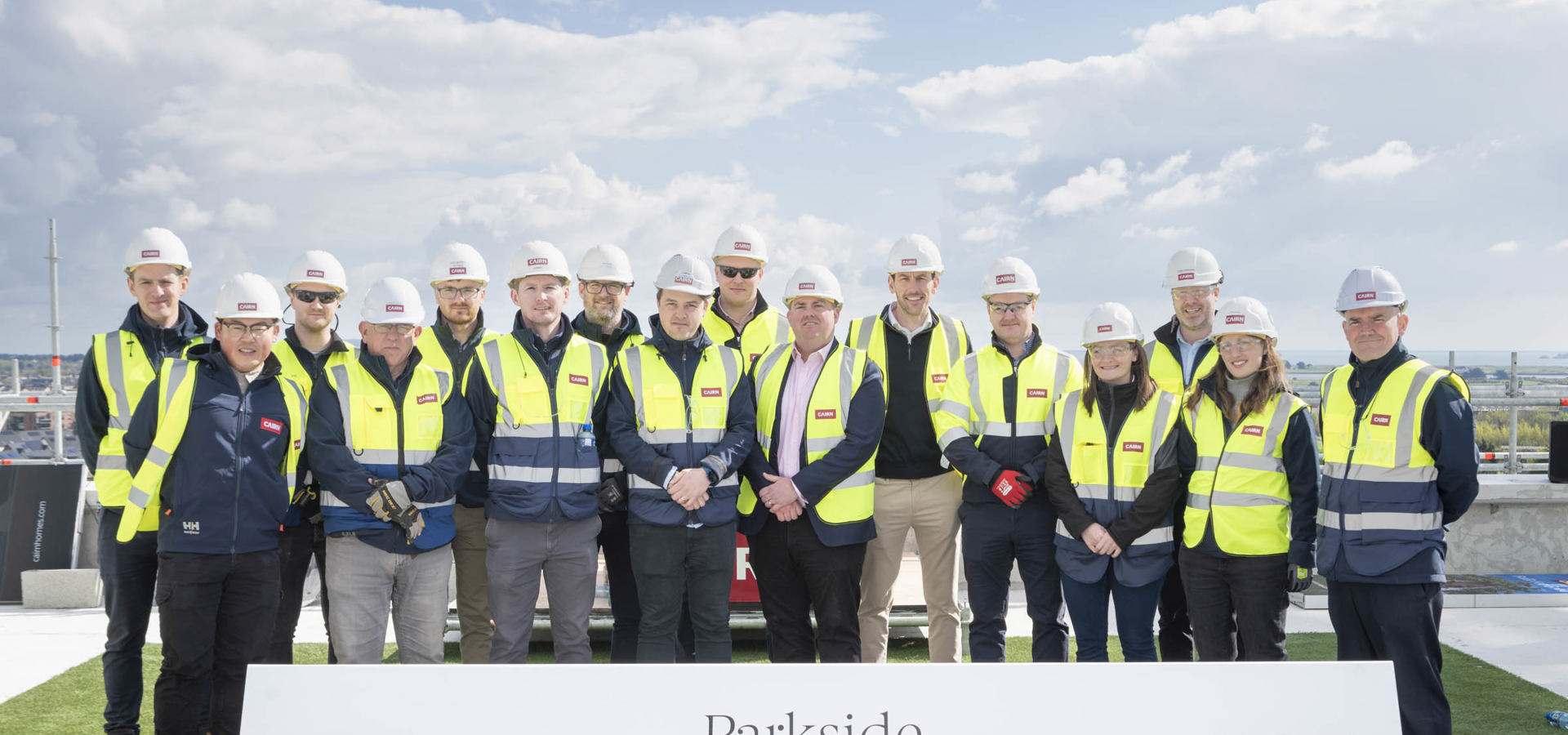 Cairn team in hi-vis and hard hats behind the Parkside Topping Out Ceremony sign, April 2024