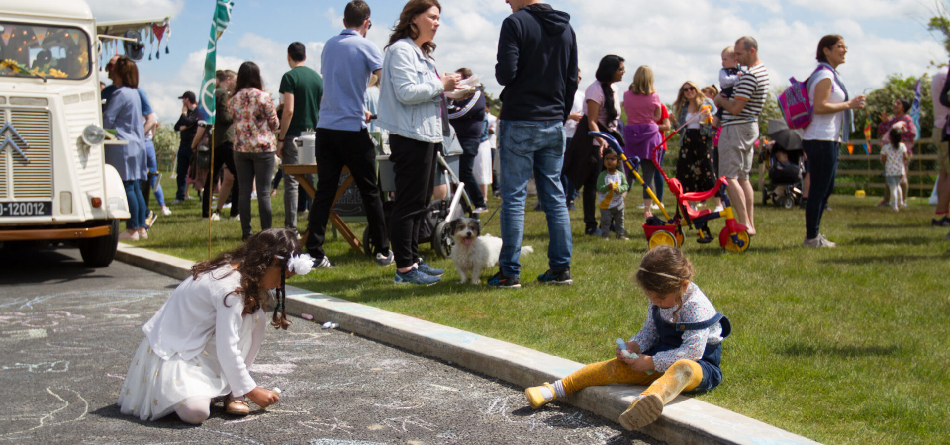 Families at a Home Together community event with a vintage van, as children draw on the path in chalk