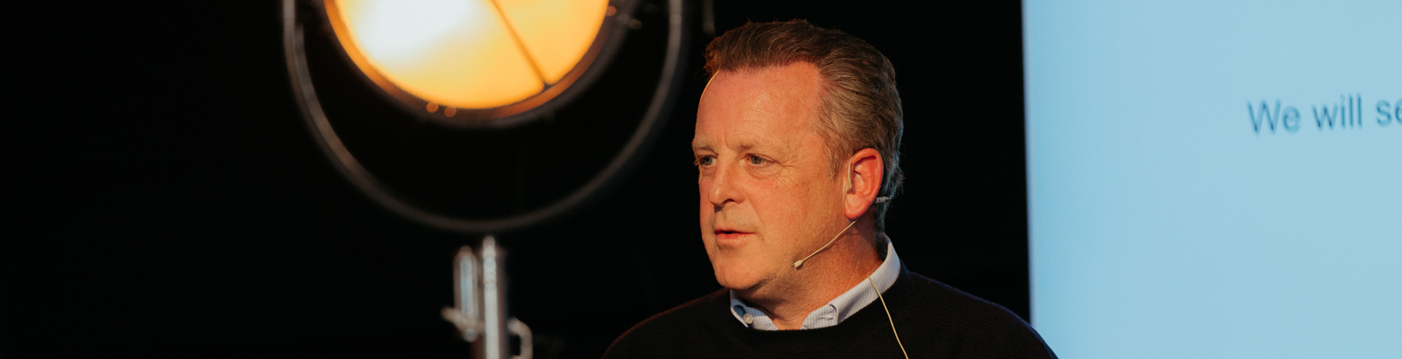 Man speaking at a lectern under a spotlight at Cairn's 2021 subcontractor evening