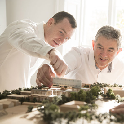 Three architects examining and measuring a detailed scale model of a building site.