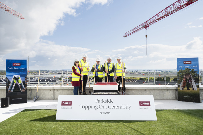 Cairn team in hi-vis behind a 'Parkside Topping Out Ceremony' sign on a rooftop